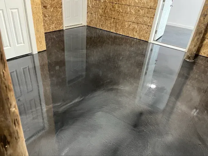 Shiny, dark gray epoxy floor in a room with unfinished wood walls and doorways.
