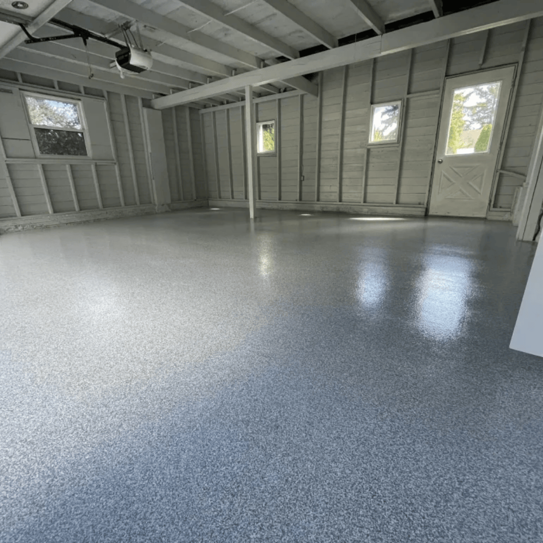 A finished, gray epoxy floor in an empty garage with white walls, ceiling, and trim; windows and a door are visible.