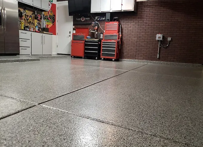 Garage with gray speckled epoxy floor, red tool chests, and brick wall.