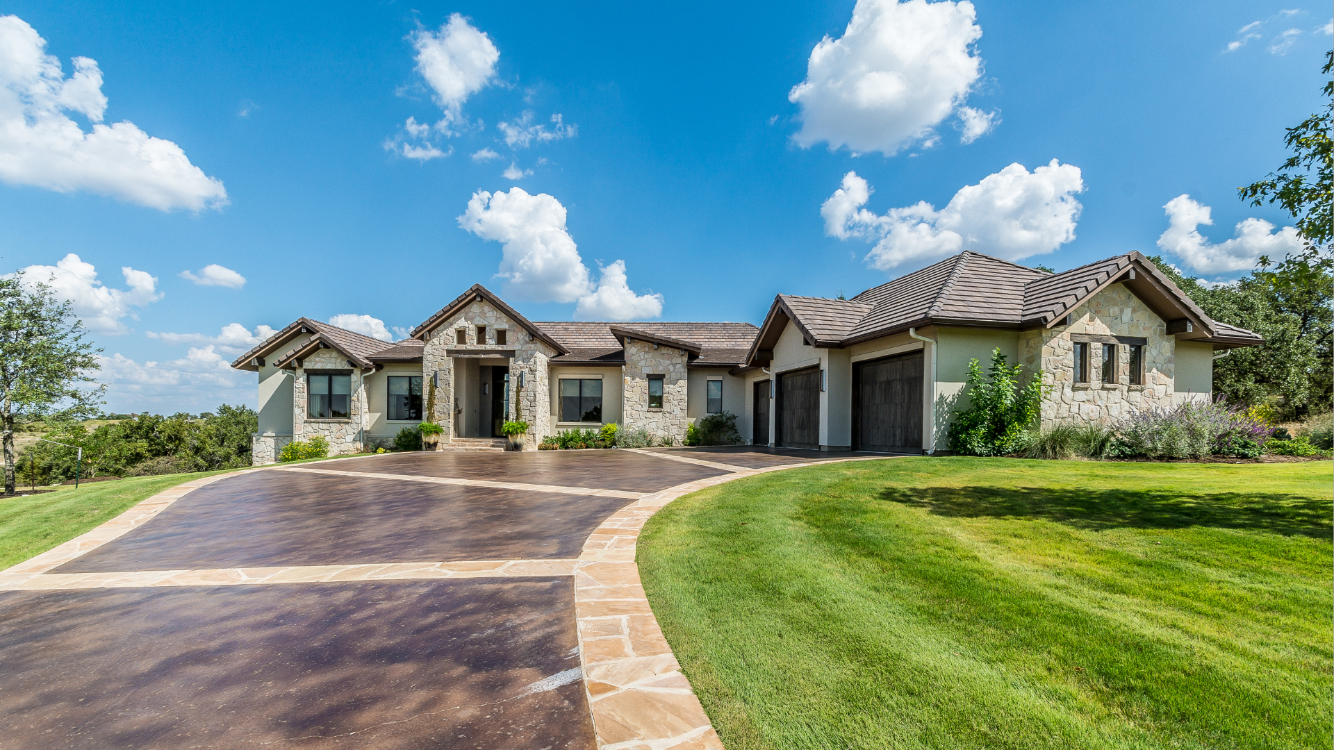 Large stone house with long driveway on a sunny day.