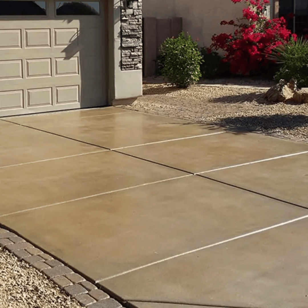 Tan concrete driveway with a garage, gravel landscaping, and blooming red flowers.