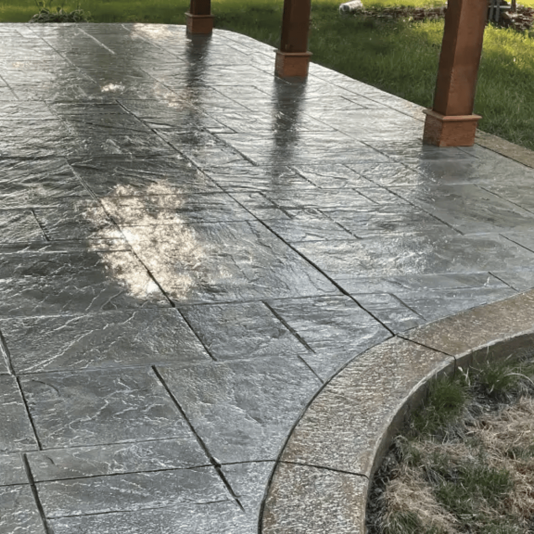 Gray stamped concrete patio with curved border and wooden posts.
