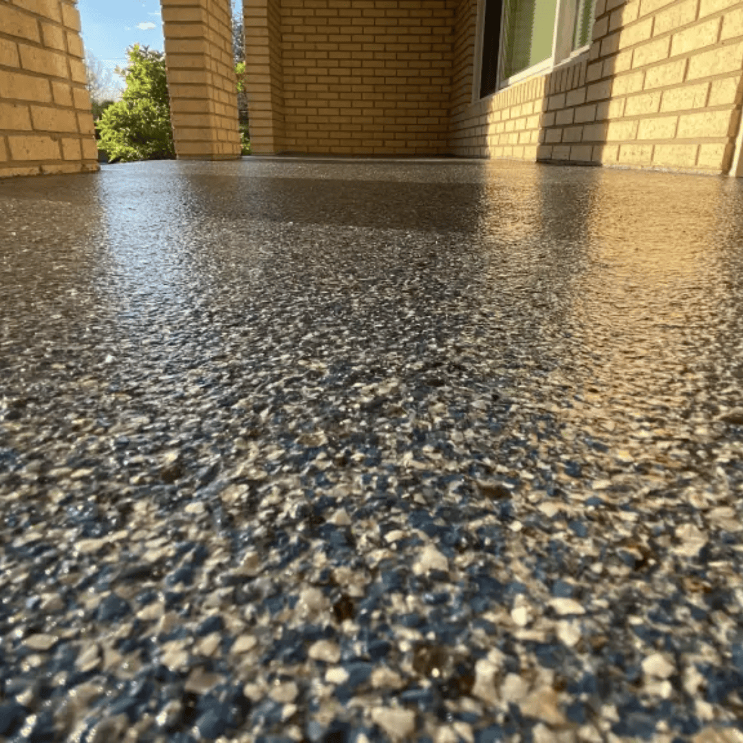 Close-up of a speckled, gray and black concrete floor on a covered porch, reflecting sunlight.