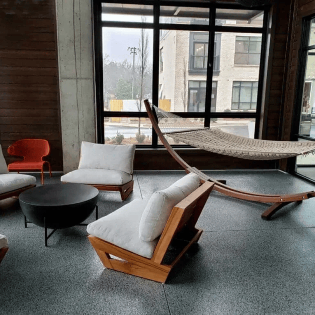 Lounge area: modern chairs, black coffee table, hammock, large window with view of a building on a rainy day.