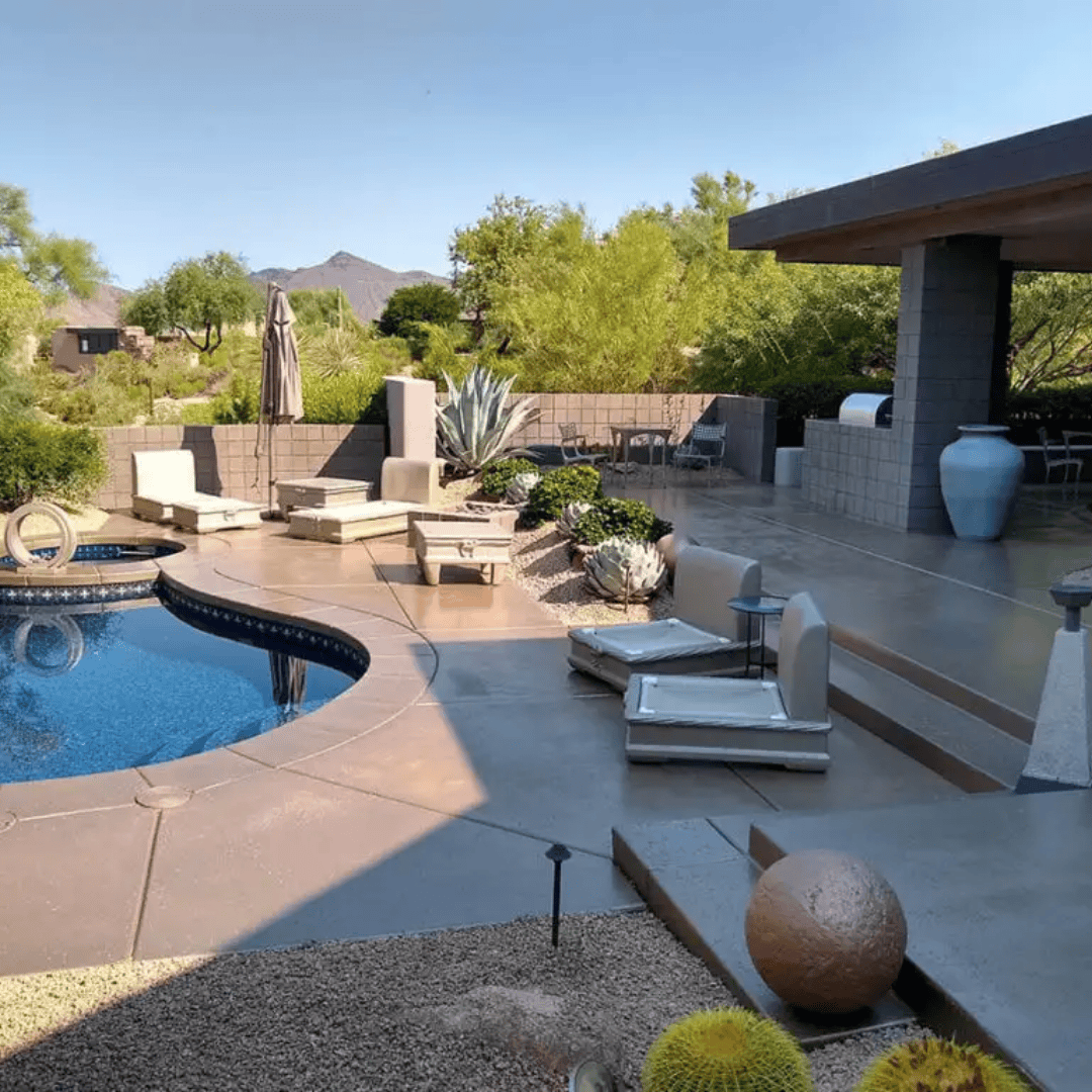 Poolside patio with lounge chairs, large vase, and landscaping under a sunny sky.