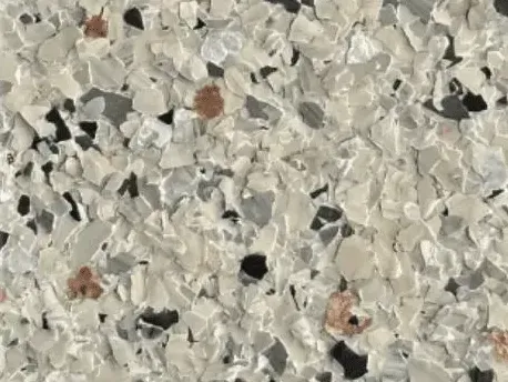 Close-up of a speckled floor coating, primarily white with gray, black, and orange flecks.