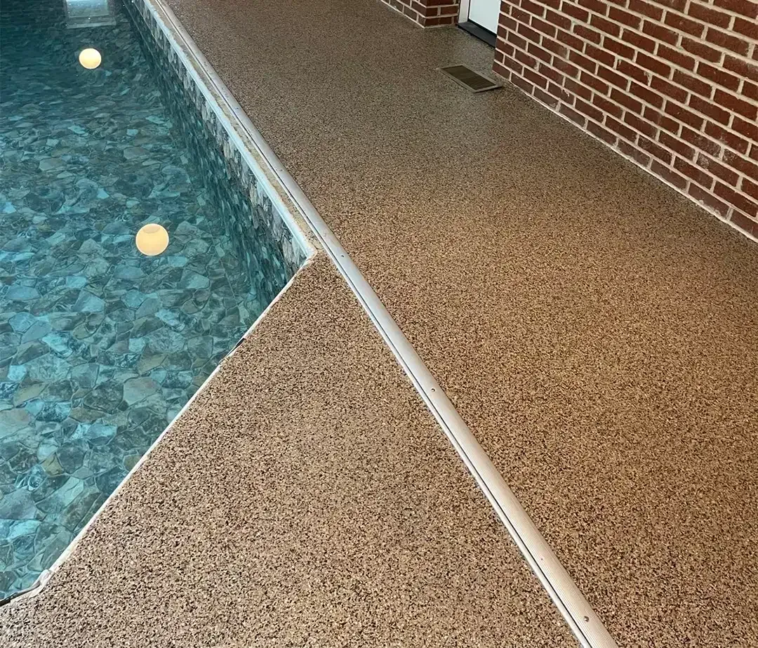 Poolside with speckled brown flooring and brick wall. Pool water is blue-green.