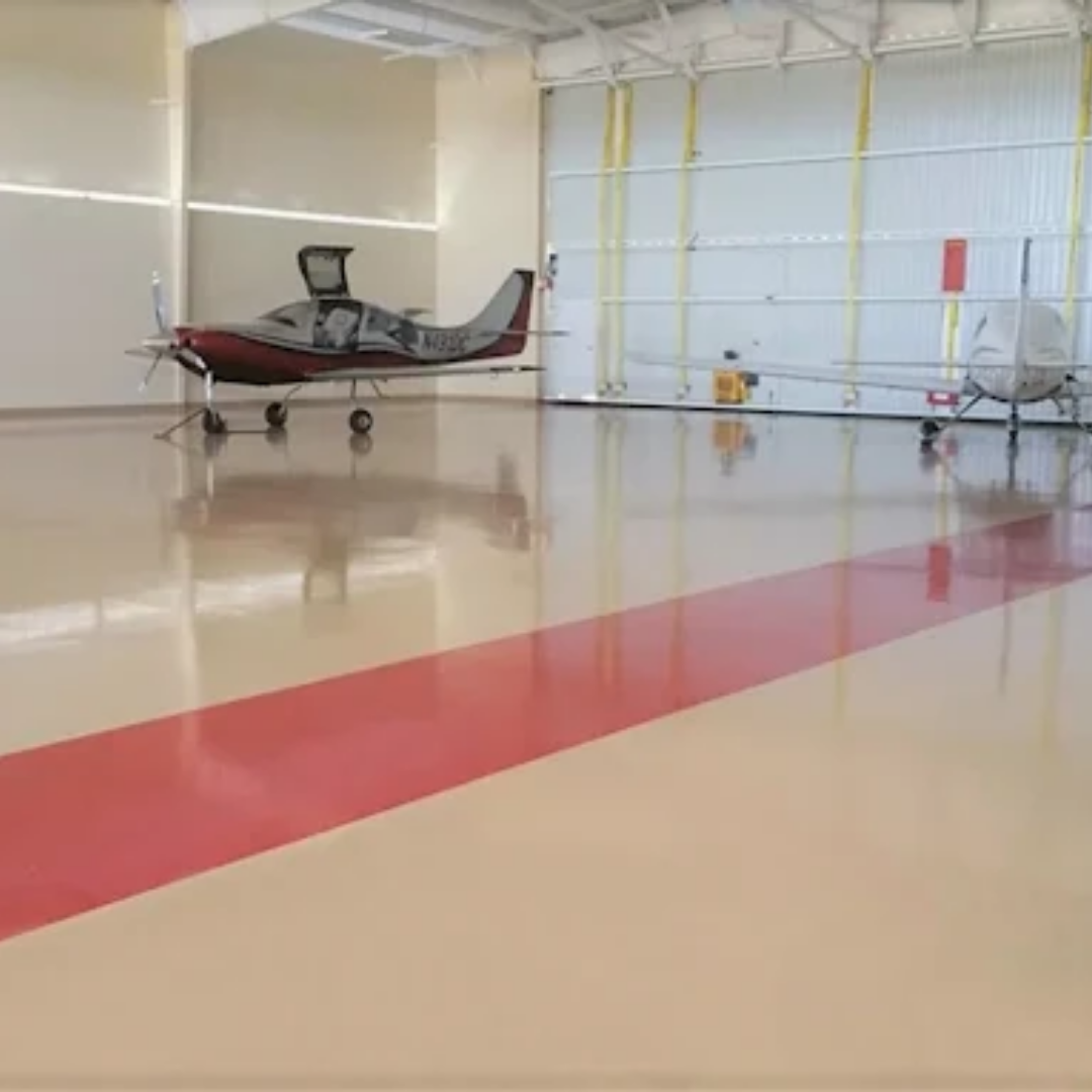 Aircraft hangar interior with two planes, red and beige floor, red stripe, open door.