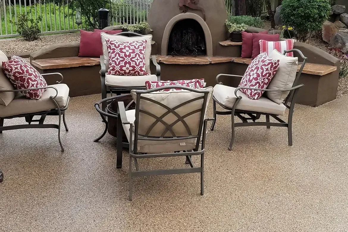 Patio with seating around a fire pit, bench seating with cushions and fireplace in background.