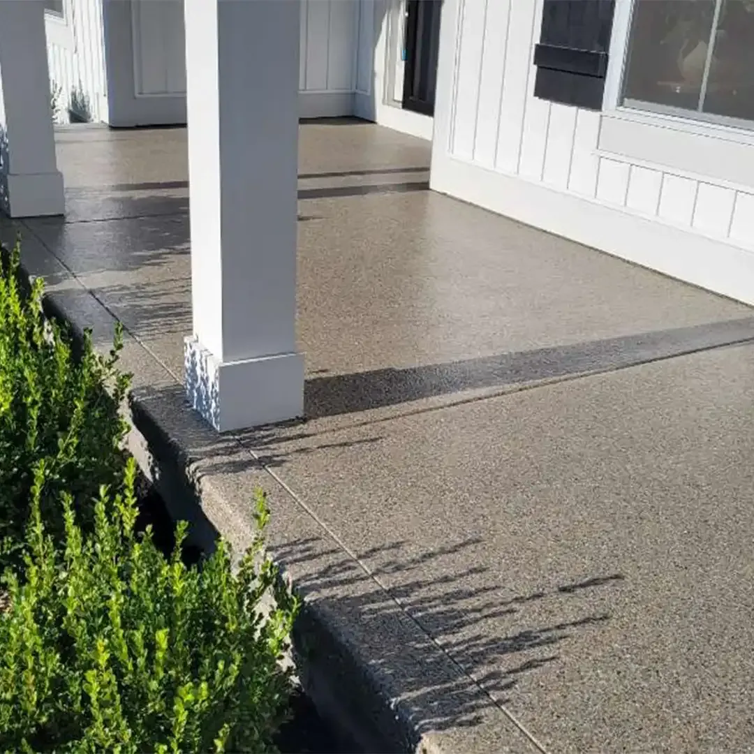 Covered porch with white pillars and gray speckled concrete. Shadow of greenery.