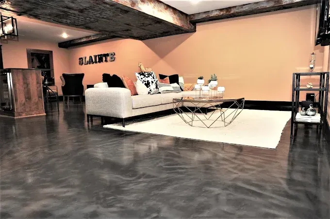 Room with a sectional sofa, coffee table, and metallic floor. Orange wall, wooden beams, and a rug.