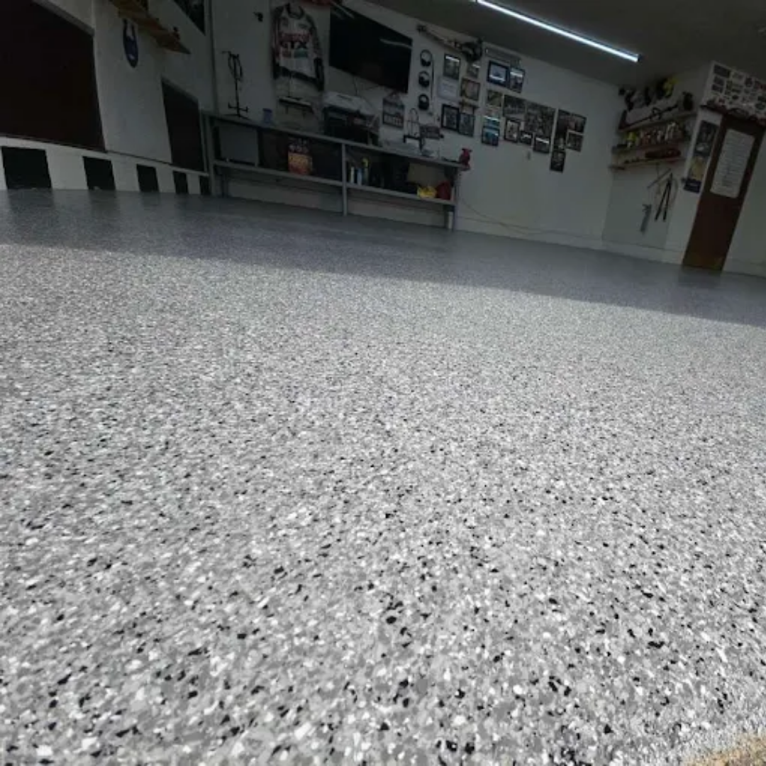 Epoxy garage floor with gray, white, and black flakes, reflecting overhead lights.
