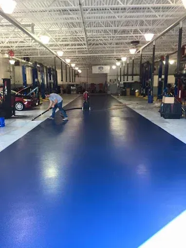 A person sweeping a shiny blue garage floor in an auto repair shop with vehicles on lifts.