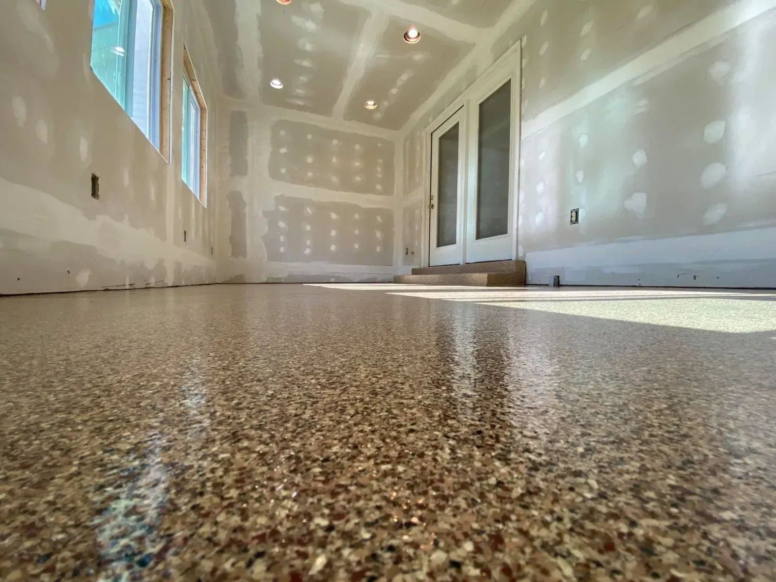 Room under construction; epoxy-coated floor, drywall walls, windows, French doors.