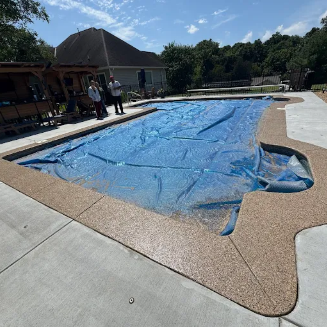Pool covered with a blue tarp; people standing nearby. Exterior shot with trees and sky.