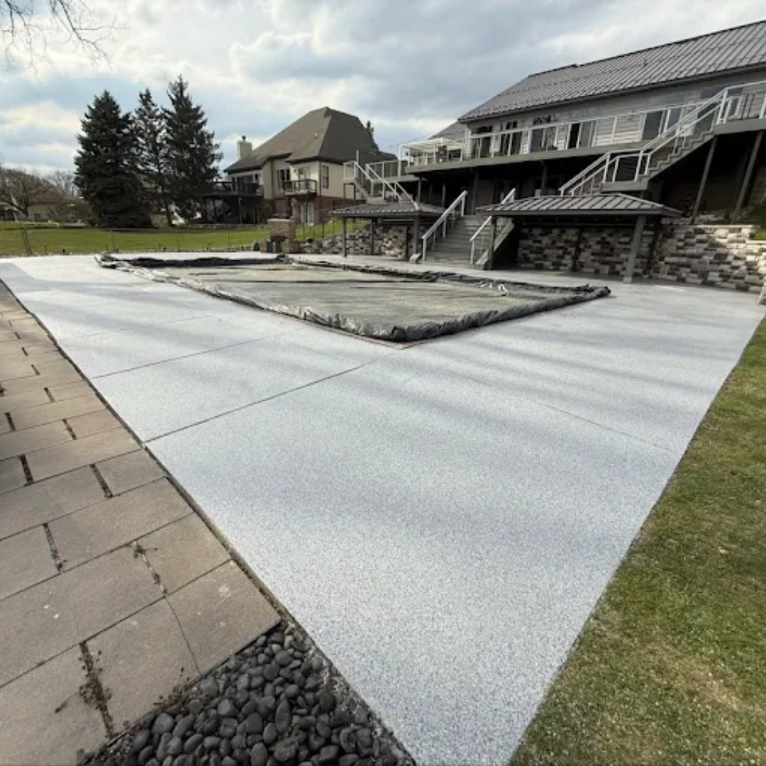 Concrete patio with covered pool, stone walkway, and a large house in the background.